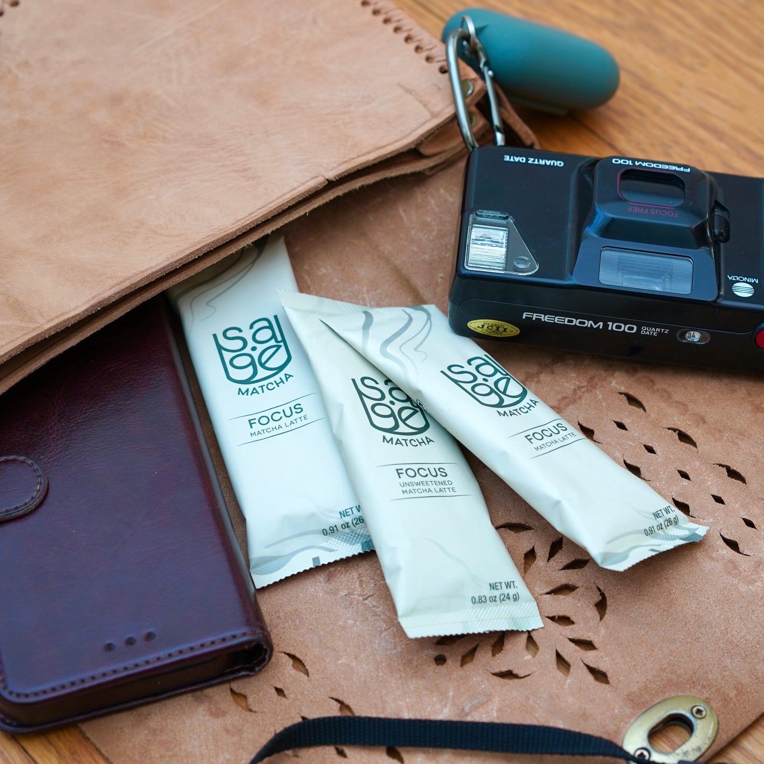 3 Focus Sage Matcha Instant Latte single serving packets, sticking out of purse, with film camera, airpods, and phone.