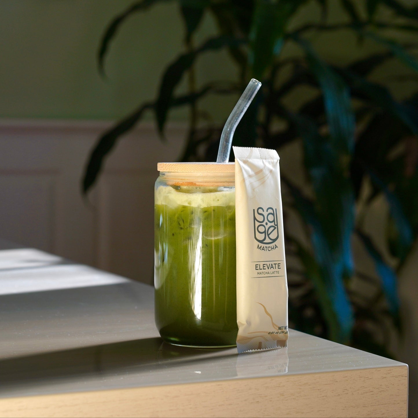 Instant Matcha Latte, Sage Matcha Elevate Blend Latte Stick against cup, on wooden tabletop. 